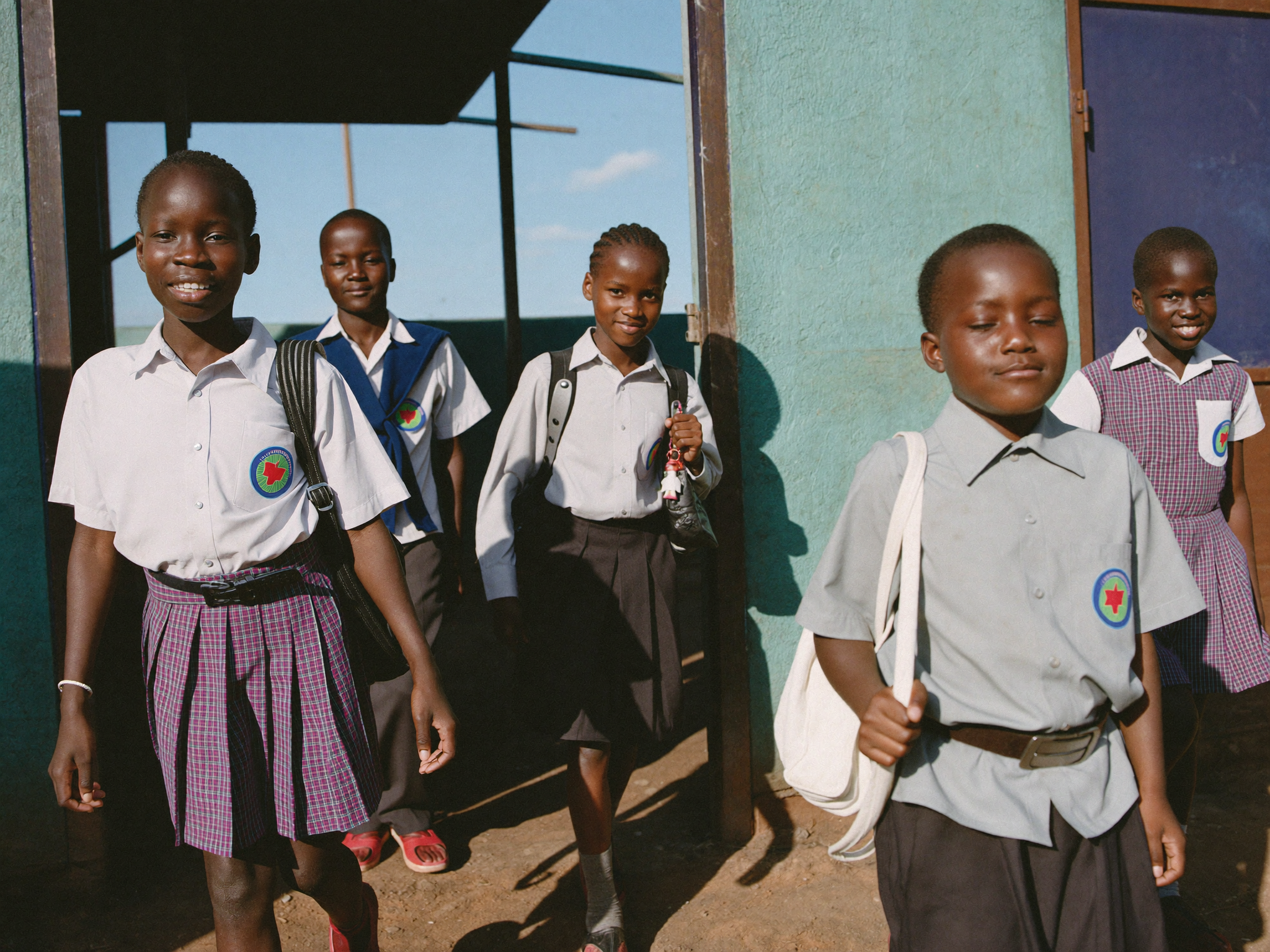 Schoolchildren in uniform walking through a school gate in Zimbabwe